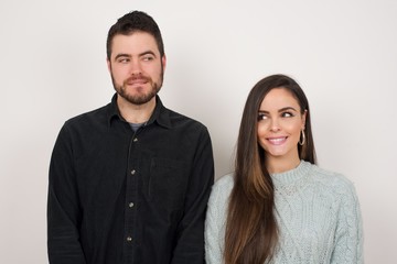 Dreamy young female with thoughtful expression, looks away keeps hands down bitting her lip thinks about something pleasant poses against gray wall.