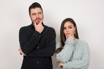Isolated portrait of stylish young European woman with hand under chin and looking sideways with doubtful and skeptical expression, worry and doubt. Standing indoors over gray background.