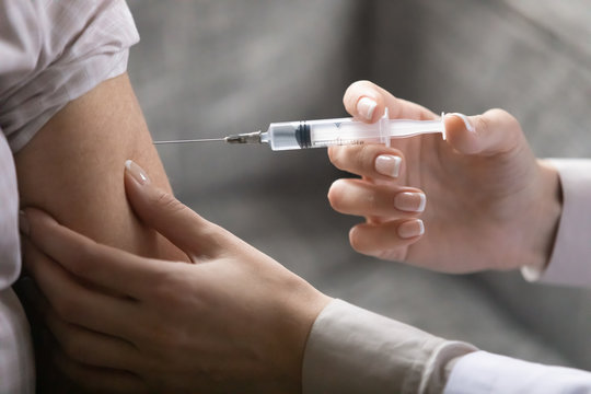 Close up image hands of nurse holding syringe makes injection to adult or elderly patient sitting on sofa indoor. Epidemic disease flu prevention, chronic illness control, health care nursing concept