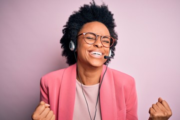 Young African American call center operator woman with curly hair using headset very happy and...