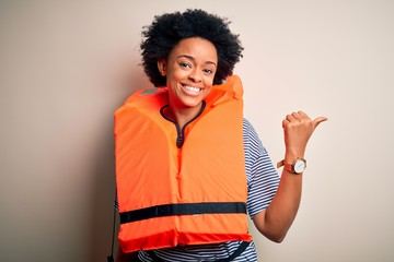 Young African American afro woman with curly hair wearing orange protection lifejacket smiling with...