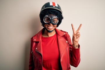 Young African American afro motorcyclist woman with curly hair wearing motorcycle helmet smiling with happy face winking at the camera doing victory sign. Number two.