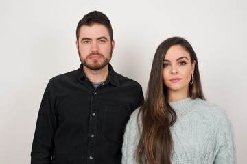 Waist up shot of joyful young woman looking to the camera, thinking or wondering about something. Both arms down, neutral facial expression.