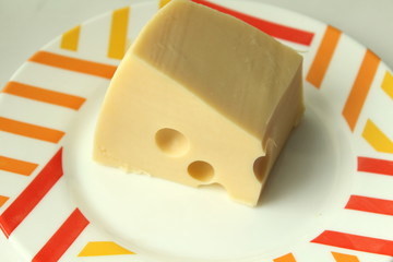 A piece of yellow cheese with holes lies on a white plate with a colored edge