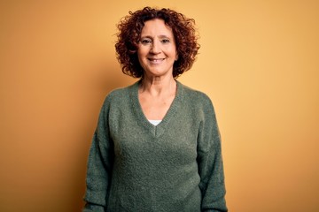 Middle age beautiful curly hair woman wearing casual sweater over isolated yellow background with a...