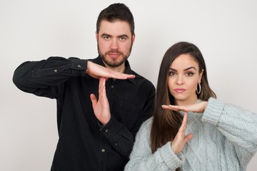 Young couple  tired and bored, making a timeout gesture, needs to stop because of work stress, time concept. Standing against gray wall.