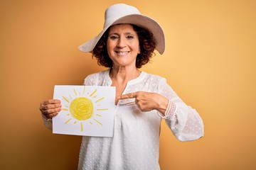 Middle age curly woman on vacation holding bunner with sun image over yellow background very happy...