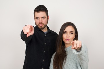 Indoor shot of cheerful young woman in casual clothes indicates happily at you, chooses to compete, has positive expression. beautiful clever student makes choice, isolated on gray Wall