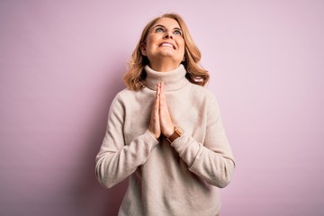 Middle age beautiful blonde woman wearing casual turtleneck sweater over pink background begging...