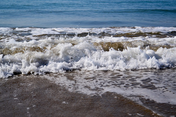 Waves with foam close up on a tropical sandy beach on a sunset. Copy space for background