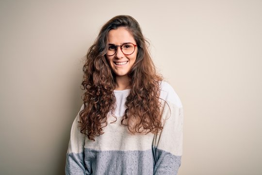 Young beautiful woman with curly hair wearing sweater and glasses over white background with a happy and cool smile on face. Lucky person.