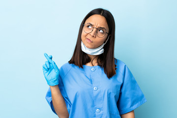 Surgeon woman over isolated blue background with fingers crossing and wishing the best