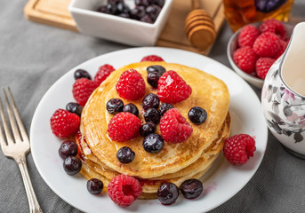 Sweet homemade pancakes with raspberries and blueberries on white plate.