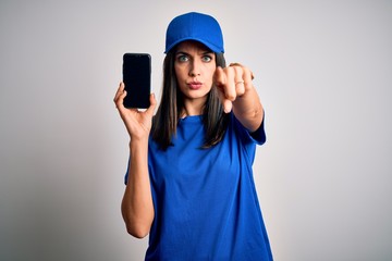 Young delivery woman with blue eyes wearing cap holding smartphone pointing with finger to the camera and to you, hand sign, positive and confident gesture from the front