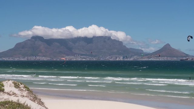Timelapse of the Table Mountain with a big cloud above on a windy day with kitesurfers in front