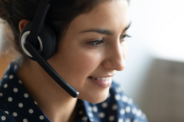 Close up head shot smiling friendly Indian woman wearing headset working online, female call center...