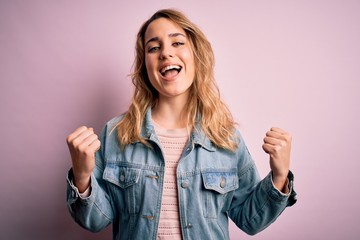 Young beautiful blonde woman wearing casual denim jacket standing over pink background celebrating surprised and amazed for success with arms raised and open eyes. Winner concept.