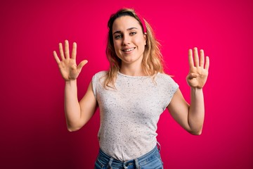 Young beautiful blonde woman wearing casual t-shirt standing over isolated pink background showing...