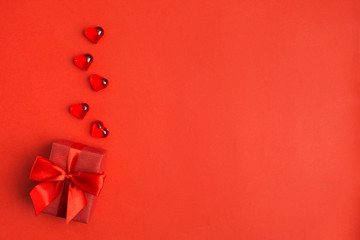 Red gift box with red bow with red hearts over red background with copy space
