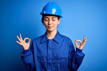 Young beautiful worker woman with blue eyes wearing security helmet and uniform relax and smiling with eyes closed doing meditation gesture with fingers. Yoga concept.