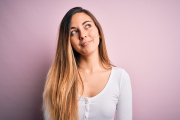 Fototapeta premium Young beautiful blonde woman with blue eyes wearing white t-shirt over pink background smiling looking to the side and staring away thinking.