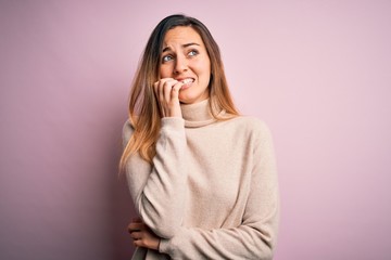 Beautiful blonde woman with blue eyes wearing turtleneck sweater over pink background looking stressed and nervous with hands on mouth biting nails. Anxiety problem.