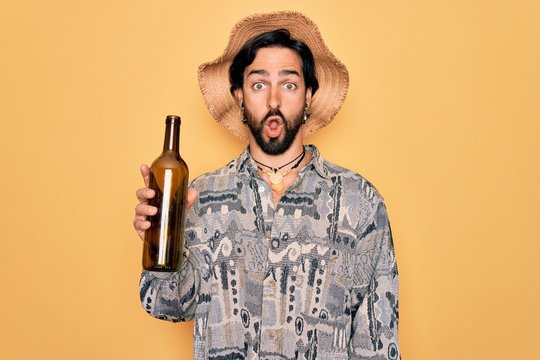 Young Handsome Hispanic Bohemian Hipster Man With Bear Drinking From A Empty Wine Bottle Scared In Shock With A Surprise Face, Afraid And Excited With Fear Expression