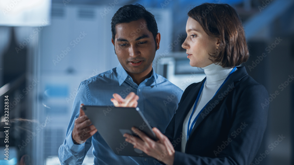 Fototapete In Technology Research Facility: Female Project Manager Talks With Chief Engineer, they Consult Tablet Computer. Team of Industrial Engineers, Developers Work on Engine Design Using Computers