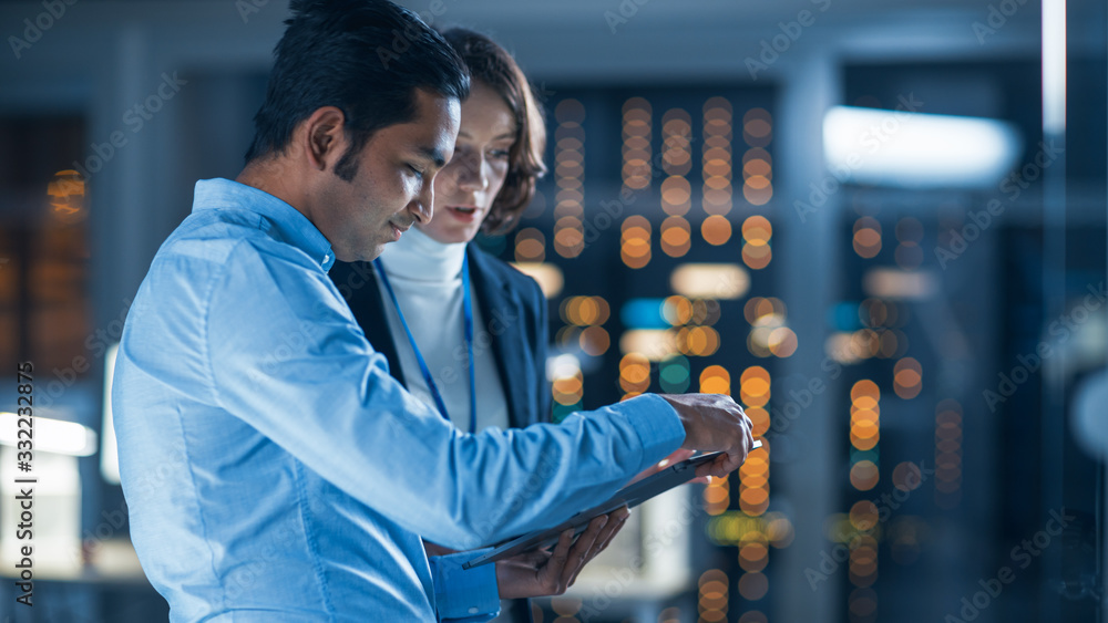 Poster In Technology Research Facility: Female Project Manager Talks With Chief Engineer, they Consult Tablet Computer. Team of Industrial Engineers, Developers Work on Engine Design Using Computers