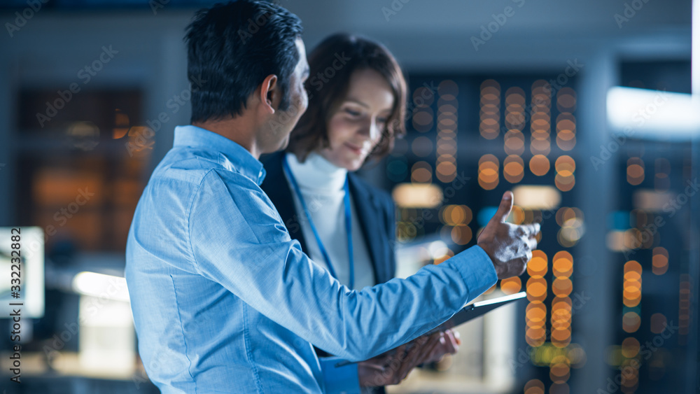 Poster In Technology Research Facility: Female Project Manager Talks With Chief Engineer, they Consult Tablet Computer. Team of Industrial Engineers, Developers Work on Engine Design Using Computers