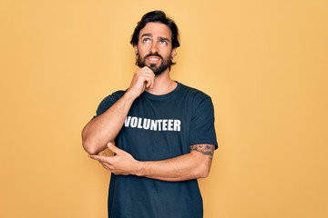 Young handsome hispanic volunteer man wearing volunteering t-shirt as social care with hand on chin thinking about question, pensive expression. Smiling and thoughtful face. Doubt concept.