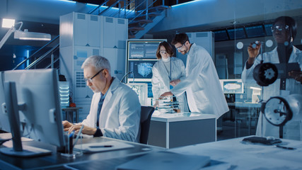 Diverse International Team of Industrial Scientists and Engineers Wearing White Coats Working on Heavy Machinery Design in Research Laboratory. Professionals Using Computers and Talking