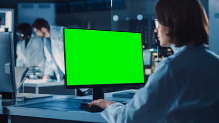 Over the Shoulder Shot: Female IT Scientist Uses Green Mock-up Screen Computer. In the Background...