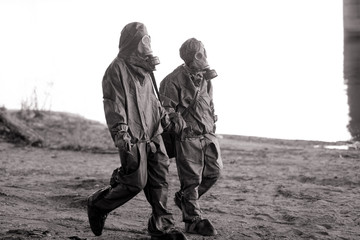 Two persons walks in NBC protective suits and gas masks.