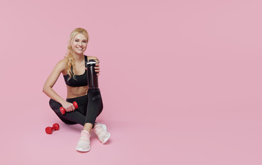 Advertisement personal training. a young sporty woman drinks a protein shake from a shaker after training indoors. Pink background