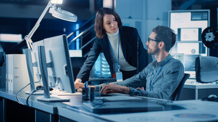 Futuristic Machine Engine Development Engineer Working on Computer at His Desk, Talks with Female...
