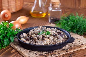 Stewed eggplant with vegetables and sour cream in a pan on a wooden table