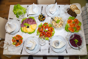 Festive set table with plates of salads, appetizer of vegetables and fruits, sliced sausage cheese, top view. Holiday, food, serving.