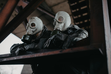 Couple in love stands under bridge in NBC protective suits and gas masks.