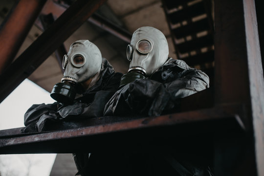 Couple in love stands under bridge in NBC protective suits and gas masks.