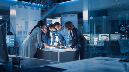 Engineers Meeting in Technology Research Laboratory: Engineers Scientists and Developers Gathered Around Illuminated Conference Table, Talking and Finding Solution, Inspecting Industrial Engine Design