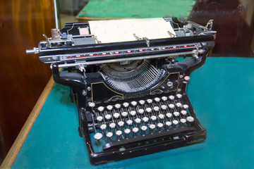 An old black typewriter standing on a blue cloth table. Antiques, appliances, technology.