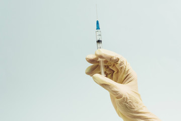 Doctor's hand in a white rubber glove holds a medical syringe on a blue background. The concept of medicine and medical care for the patient