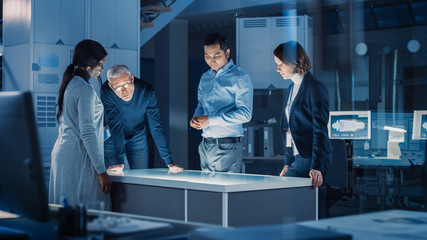 Professionals Meeting in Virtual Reality Content Design Creative Lab: Engineers, Scientists and Game / App Developers Gathered Around Illuminated Interactive Table. Specialists Talking, Gesticulating