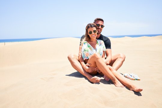 Young beautiful couple smiling happy and confident. Sitting with smile on face hugging at the beach