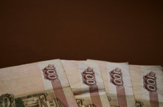 bills of one hundred rubles on a brown background are laid out by a fan of the krp plan