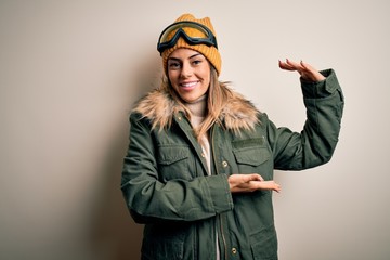 Young brunette skier woman wearing snow clothes and ski goggles over white background gesturing with hands showing big and large size sign, measure symbol. Smiling looking at the camera. Measuring