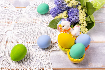 Easter composition with colorful eggs in a ceramic stand-rabbit and spring bouquet with purple and yellow flowers on a white wooden table