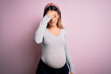 Young beautiful brunette woman pregnant expecting baby over isolated pink background tired rubbing...