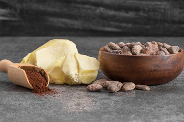 Cocoa butter or Cocoa bean solid oil with cacao powder in spoon and raw cocoa beans on rustic backdrop, healthy natural oil
